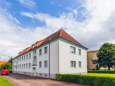 Mehrfamilienhaus mit weißer Fassade, rotem Dach und gepflegtem Vorgarten unter leicht bewölktem Himmel