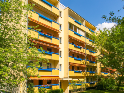 Farbenfrohes Wohngebäude mit Balkonen, umgeben von Bäumen und Grünflächen bei sonnigem Wetter