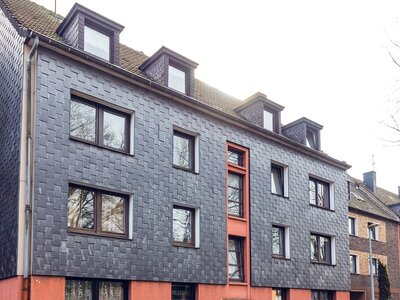 Mehrfamilienhaus mit Schieferfassade und Dachgauben bei bewölktem Himmel