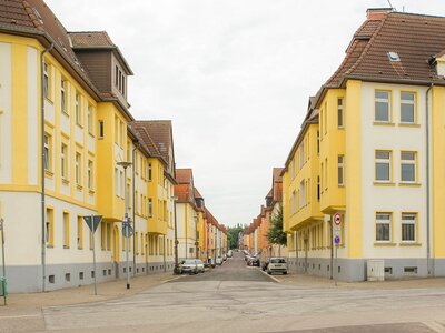 Straßenzug mit symmetrischen gelb-weißen Mehrfamilienhäusern unter bewölktem Himmel
