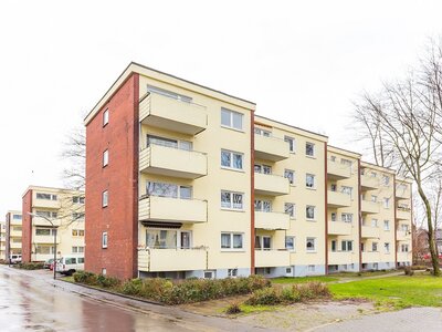 Mehrfamilienhaus mit Balkonen und Ziegelakzenten, umgeben von Grünflächen und Gehwegen bei bewölktem Wetter