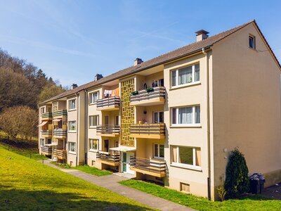 Mehrfamilienhaus mit Balkonen, umgeben von Grünflächen und Bäumen, bei sonnigem Wetter