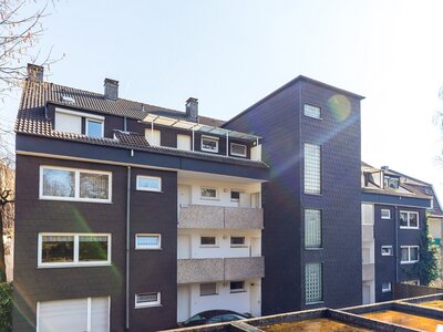 Modernisiertes Mehrfamilienhaus mit dunkler Fassade und Balkonen bei sonnigem Wetter
