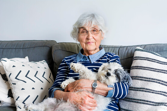 Seniorin sitzt auf der Couch mit Hund auf dem Arm