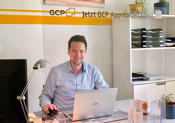 GCP Mitarbeiter lachend an seinem Schreibtisch