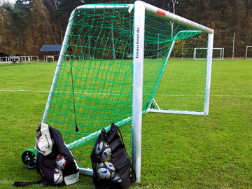 Auf einem Fußballplatz steht ein Fußballtor und davor zwei Säcke mit Fußbälle. 