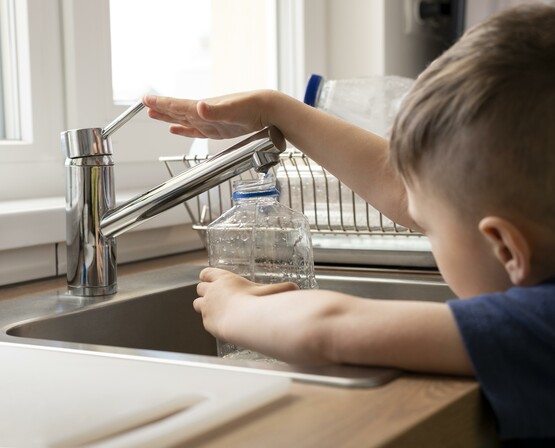 Kind füllt Wasser aus einem Wasserhahn in ein Glas